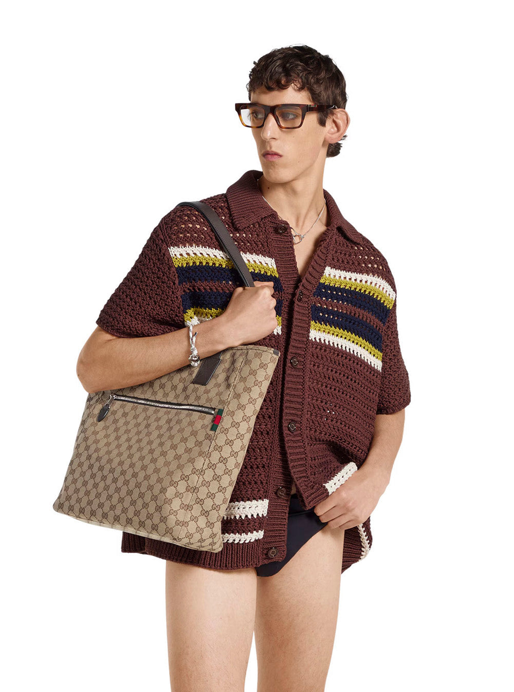 Person wearing a brown knitted poncho holding a Gucci bag on a white background