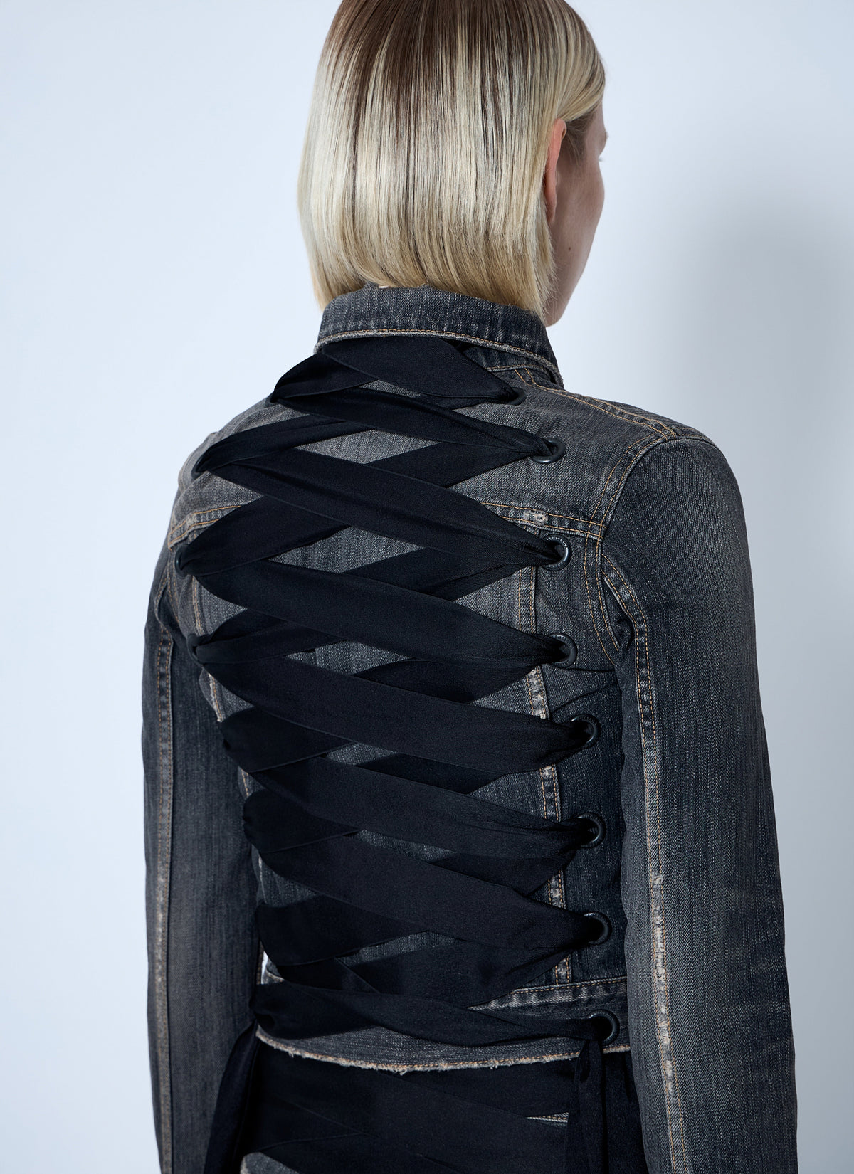 Denim jacket with black lacing on a plain background