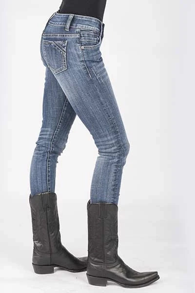 A person shown from the waist down wearing medium-wash blue skinny jeans and black leather cowboy boots against a plain white studio background.
