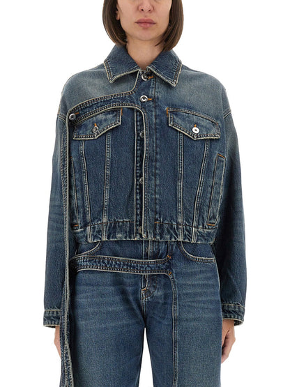 A model wearing a cropped blue denim jacket with a collar, button front, and two flap chest pockets, paired with matching blue denim bottoms against a plain white background.