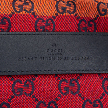 Close-up of a Gucci textile product showing the red and orange GG monogram canvas with a black leather band embossed with 'GUCCI made in Italy' and a UDIAN number.