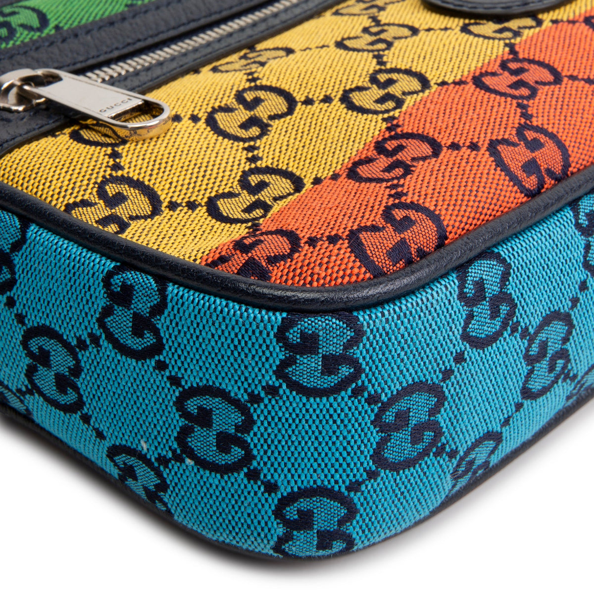 Close-up of a Gucci canvas pouch featuring the brand's interlocking GG monogram pattern in black over a vibrant rainbow stripe design of yellow, orange, and turquoise blue.