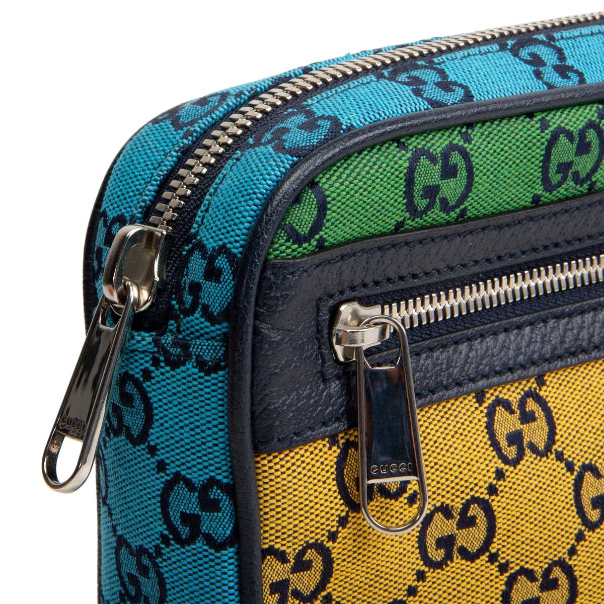 Close-up of a Gucci crossbody bag showing the signature GG monogram canvas in turquoise blue, green, and yellow panels, with dark navy leather trim and silver-tone zippers.