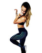 A woman posing in a black sports bra and high-waisted black leggings with glowing blue and green curved line patterns, standing in front of white wooden doors.