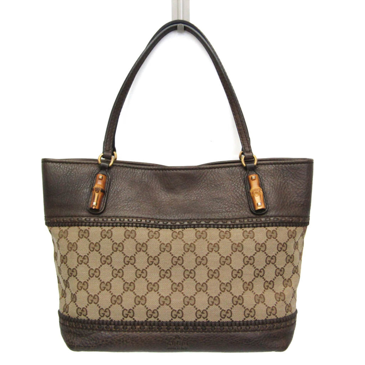 A Gucci tote bag featuring dark brown leather trim and handles, with a beige and brown GG Supreme canvas body, shown against a plain white background.