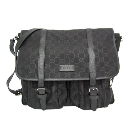 A black Gucci messenger bag featuring the brand's signature GG monogram canvas, black leather straps, and a front flap with a small metal Gucci logo plaque.