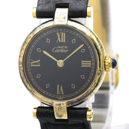 A vintage Cartier watch with a black dial, gold-tone case, and black leather strap, shown close-up against a white background.