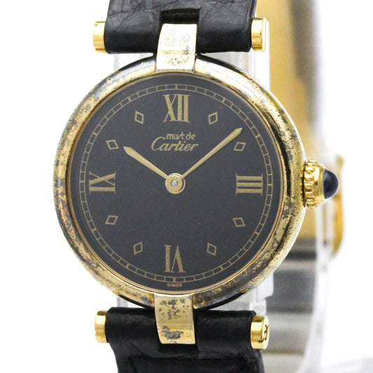 A vintage Cartier watch with a black dial, gold-tone case, and black leather strap, shown close-up against a white background.