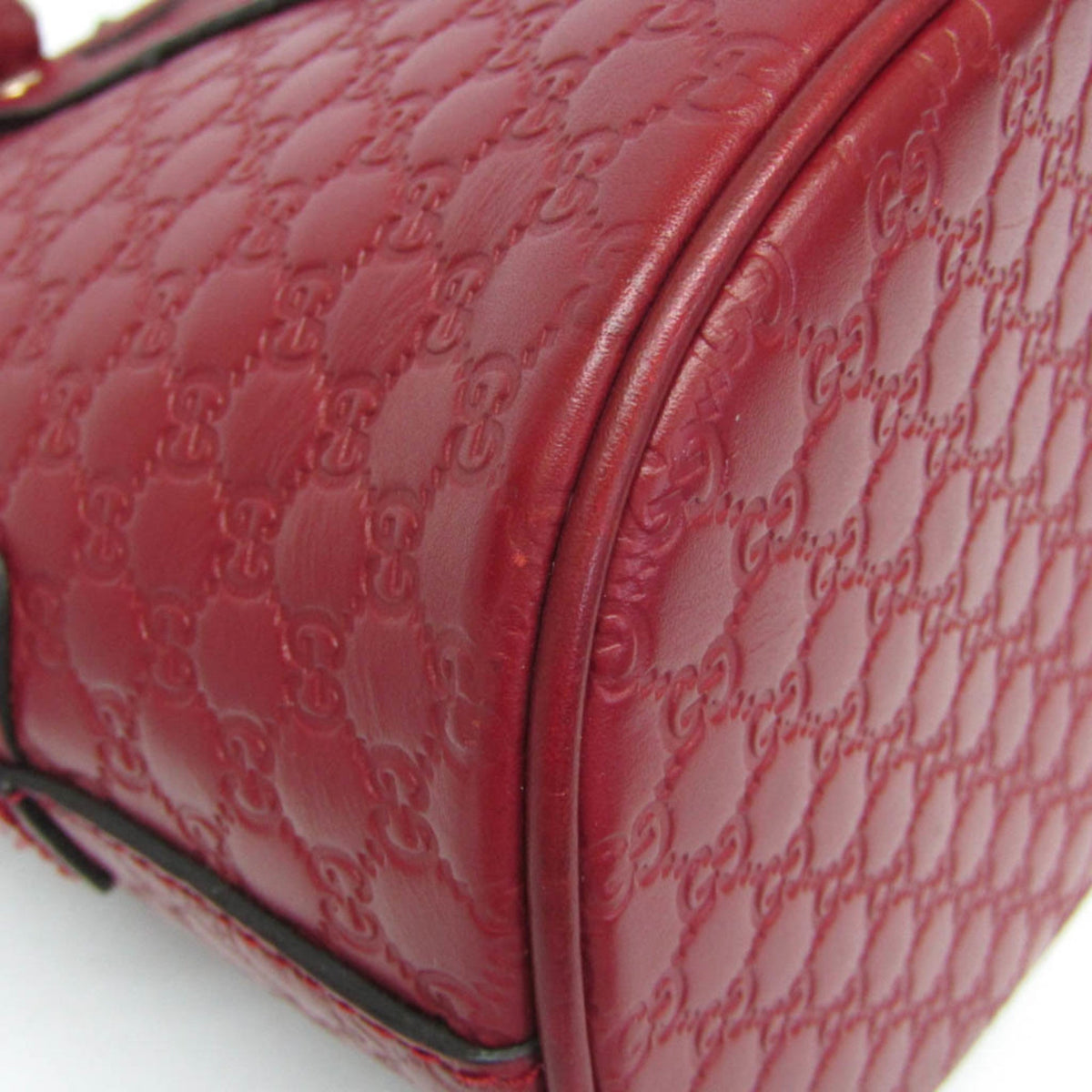Close-up of a red leather handbag featuring an embossed interlocking GG monogram pattern, showing the texture and curved corner detail.