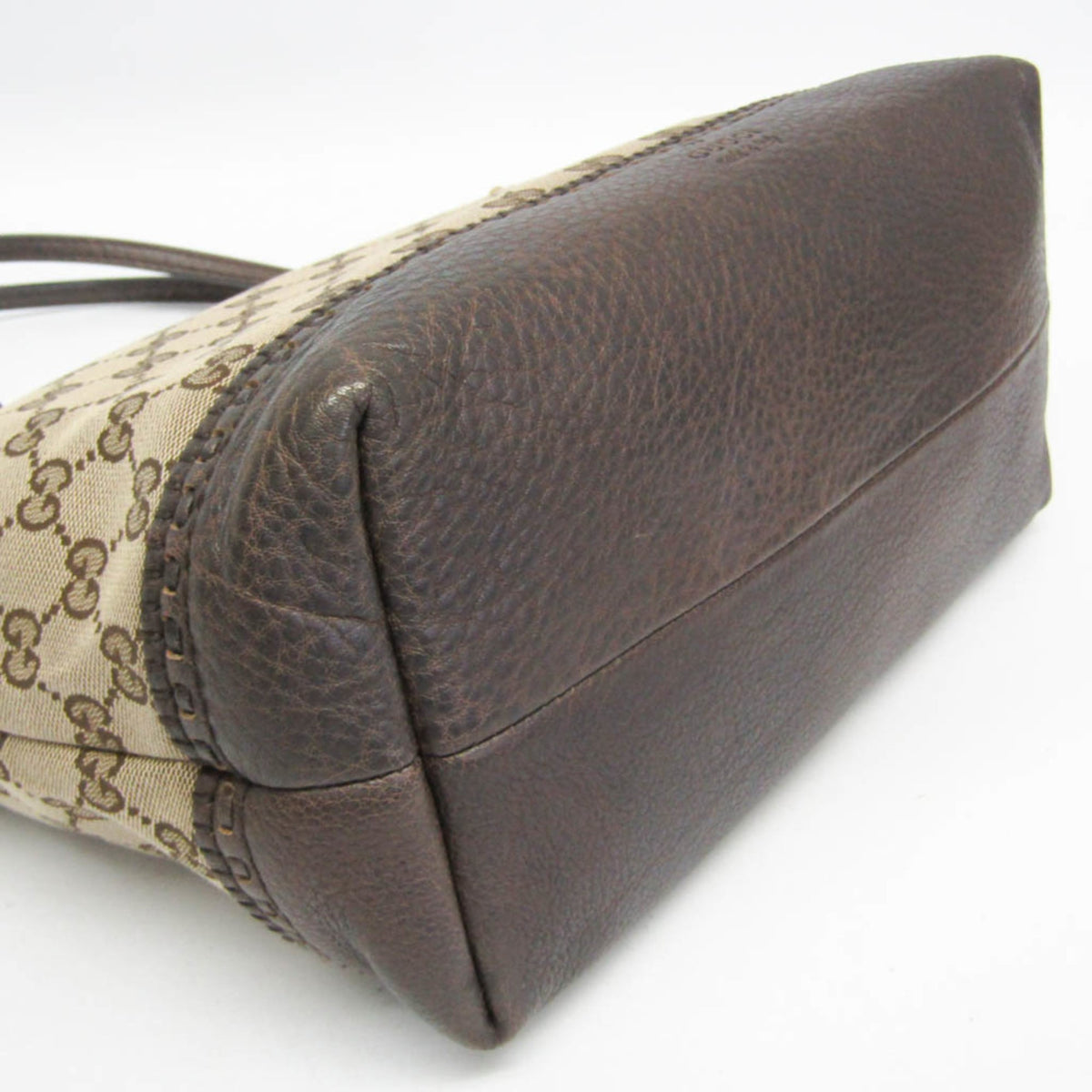 A close-up of a Gucci handbag corner showing dark brown pebbled leather and the signature beige GG monogram canvas.