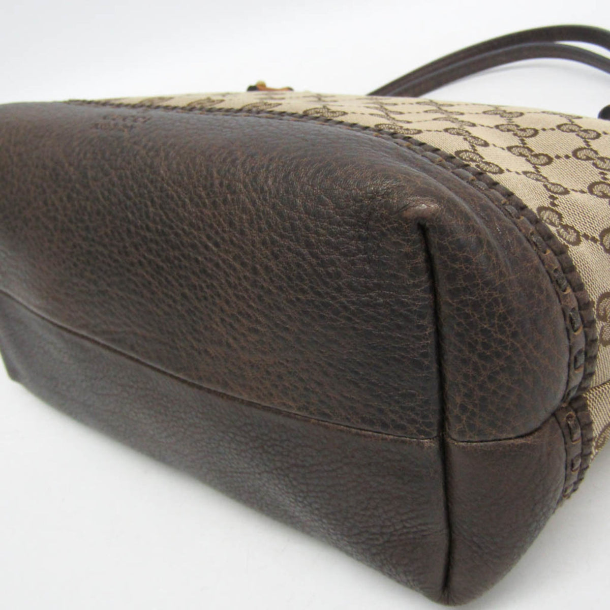 Close-up of a Gucci handbag showing the dark brown pebbled leather base and the beige GG monogram canvas upper panel with a dark strap.