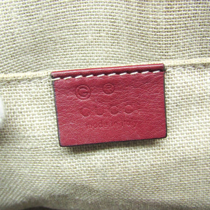 Close-up of a Gucci leather brand patch in dark red, stitched onto a beige woven canvas fabric.