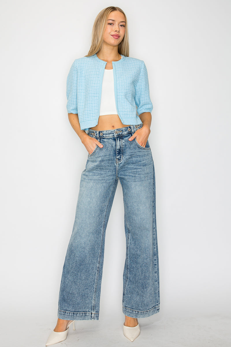 Woman wearing a light blue jacket, white top, and wide-leg jeans on a white background