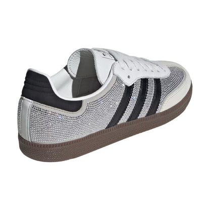 A low-top sneaker featuring a silver rhinestone-embellished upper, three black stripes on the side, white laces, a black heel tab, and a brown gum sole, shown from a three-quarters rear angle on a white background.