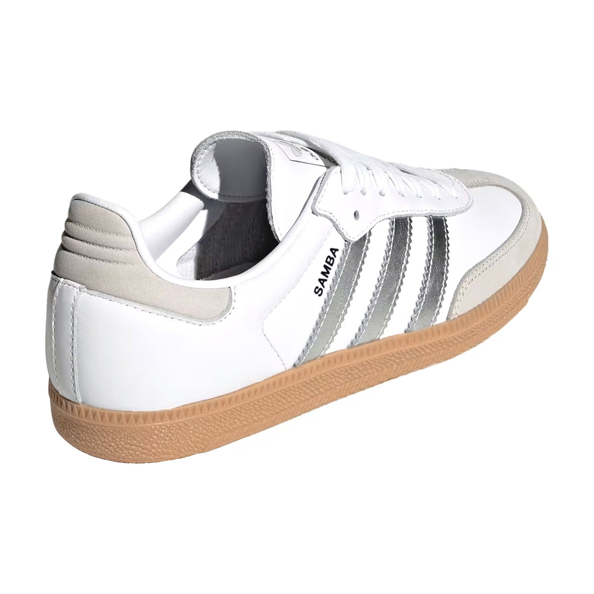 A white Adidas Samba sneaker with metallic silver stripes, a beige heel tab, and a brown gum sole, shown from a three-quarters rear angle on a white background.
