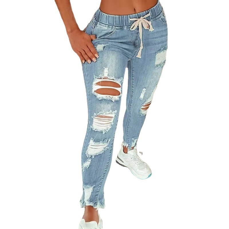 Light blue distressed skinny jeans with ripped details and a cream drawstring waistband, shown on a model against a white background.