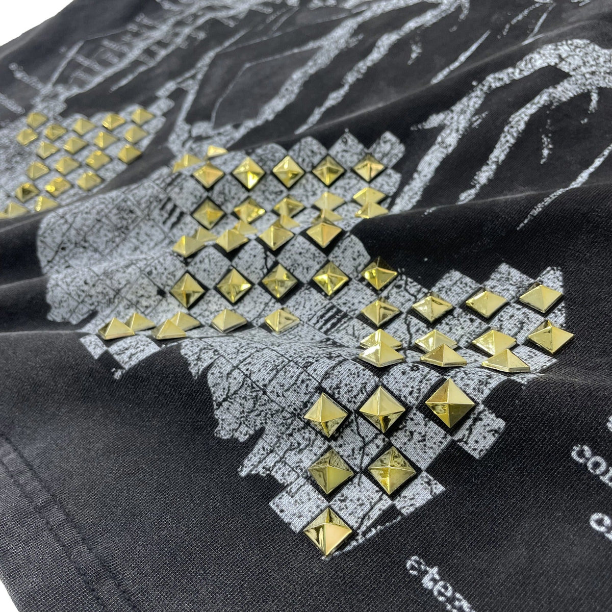 Close-up of a black graphic garment with a distressed gray map print and rows of shiny gold pyramid studs.