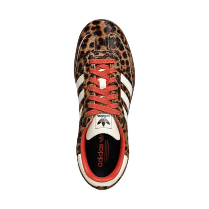 A single Adidas Samba sneaker shown from a top-down view, featuring a brown and black leopard print upper, white side stripes, white tongue and heel tabs, and coral-red laces and inner lining, set against a plain white background.