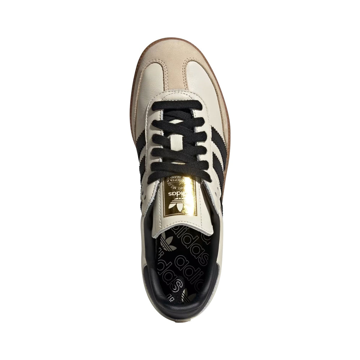 A top-down view of an Adidas Samba sneaker in cream, black, and brown, featuring a prominent gold metal tongue plate.