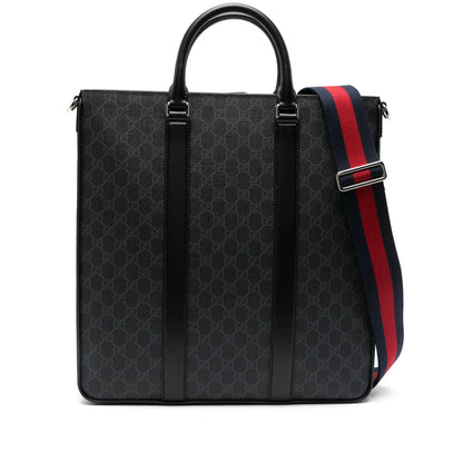 A black Gucci tote bag featuring the brand's signature GG monogram pattern, black leather trim, top handle, and a red and navy blue webbed shoulder strap with a silver metal buckle.