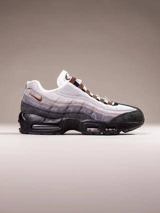 A Nike Air Max 95 sneaker in a white, gray, and black colorway with brown accents, shown in a side profile against a neutral beige background.