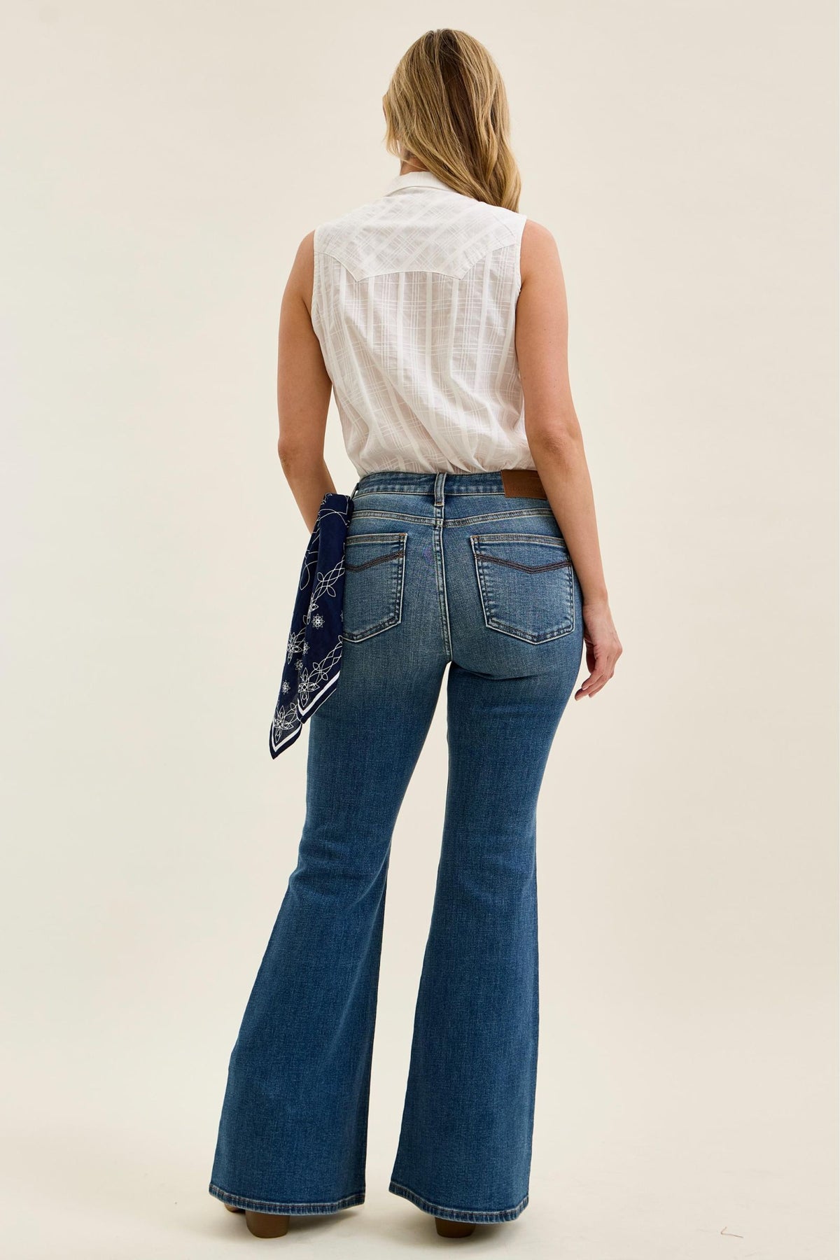 Woman wearing blue flared jeans and a white sleeveless top on a plain background