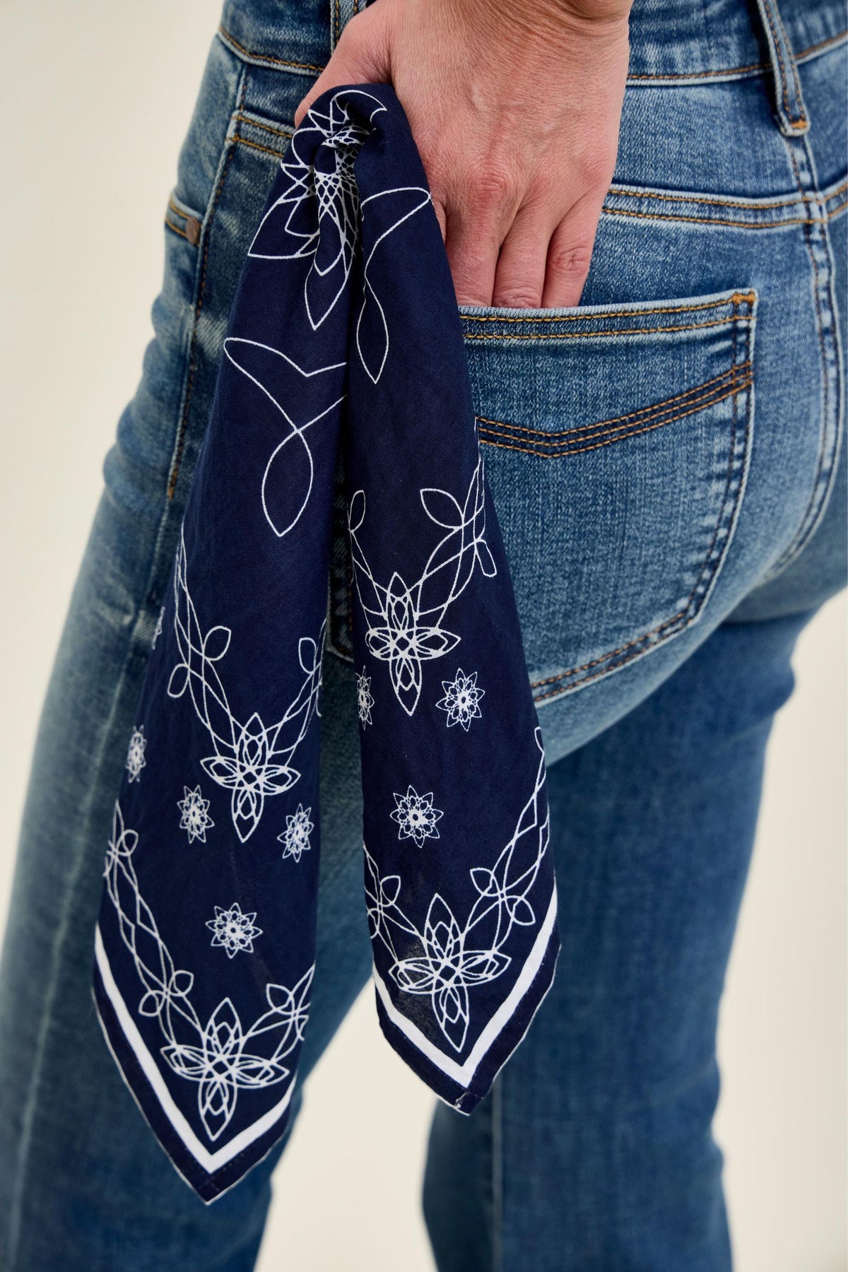 Navy blue bandana with white patterns held by a person wearing blue jeans.