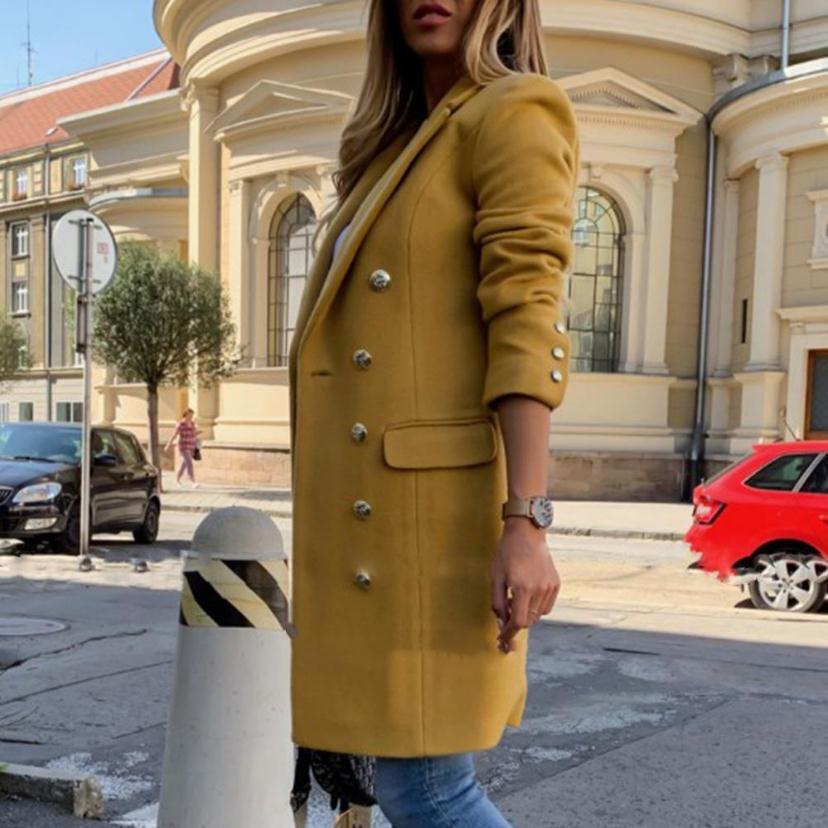 Person wearing a yellow coat standing on a street with buildings and cars in the background