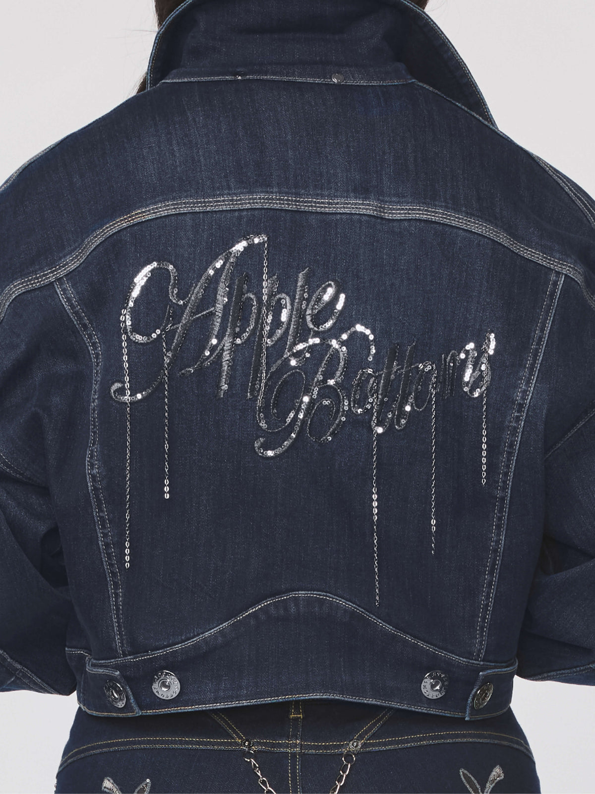 Dark denim jacket with 'Apple Bottoms' text in rhinestones on a white background