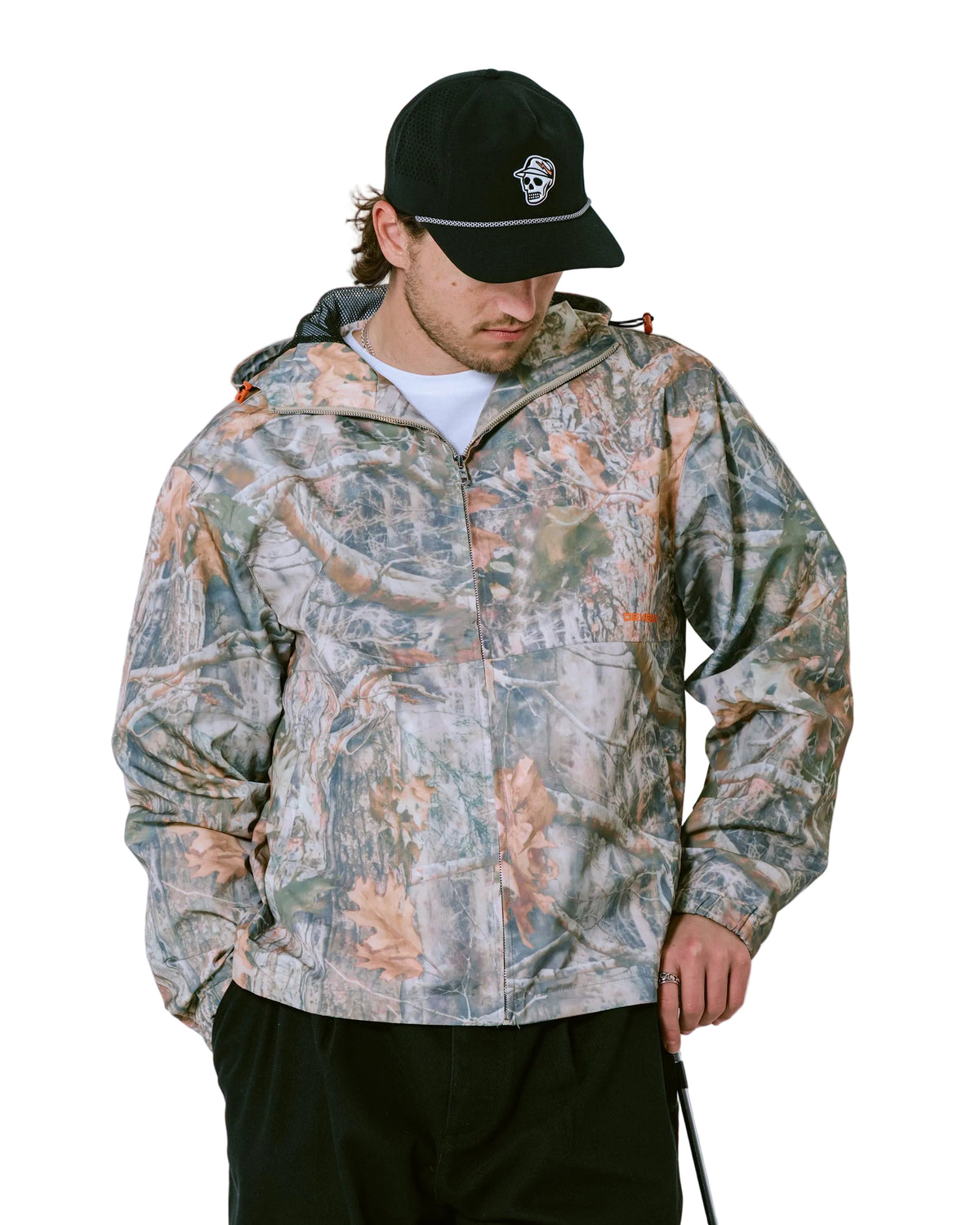 Person wearing a camouflage jacket and black cap with a skull design on a light gray background