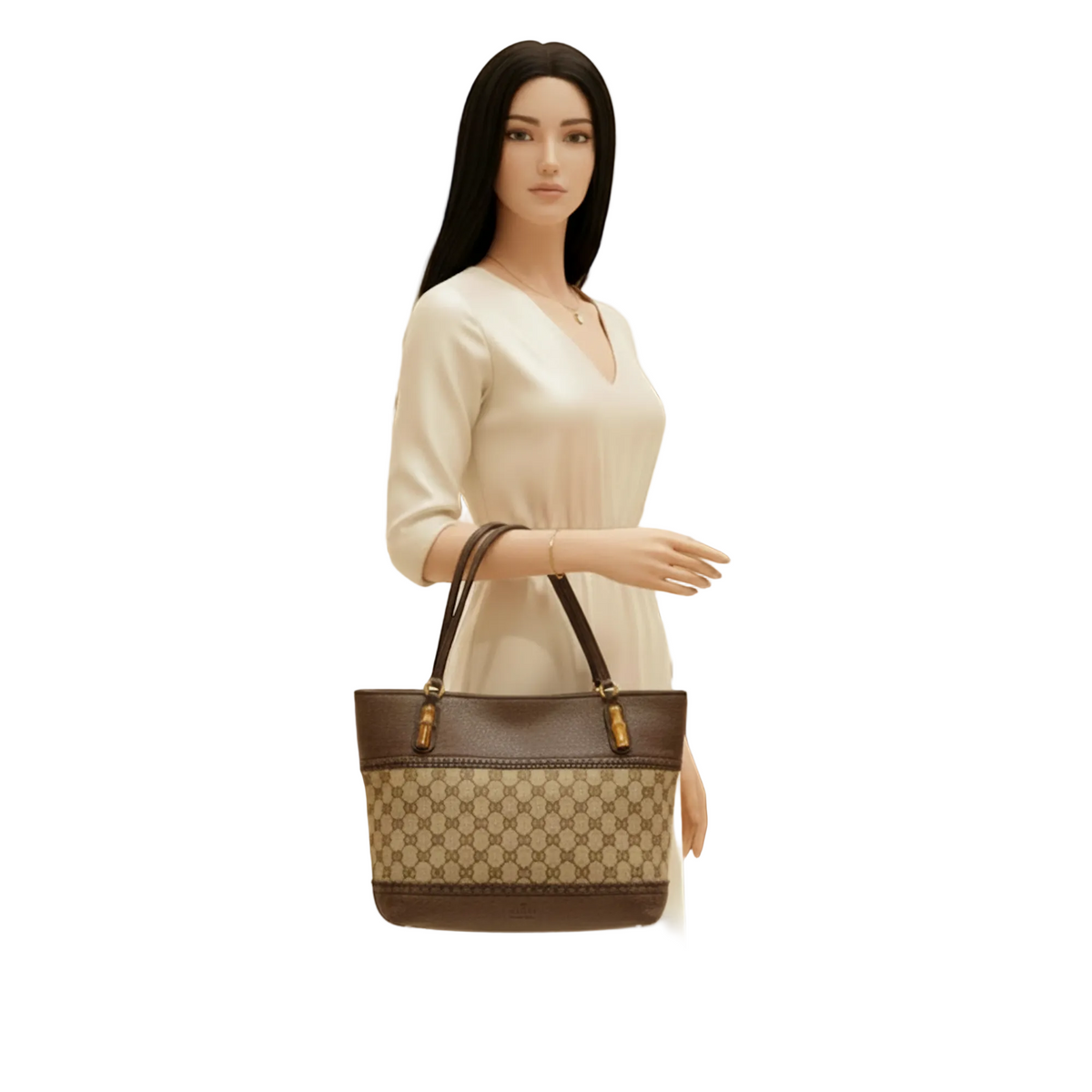 A woman in a cream dress stands inside a boutique holding a brown and beige monogram tote bag with dark brown leather handles and trim.