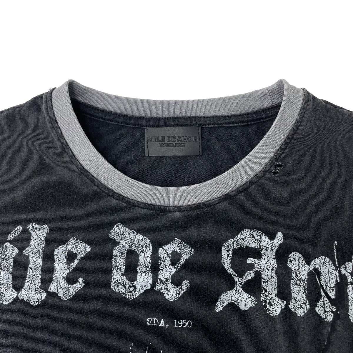 Close-up of a washed black t-shirt with a gray ribbed crew neck collar and a distressed white gothic text graphic reading 'ile de Ang' across the chest.