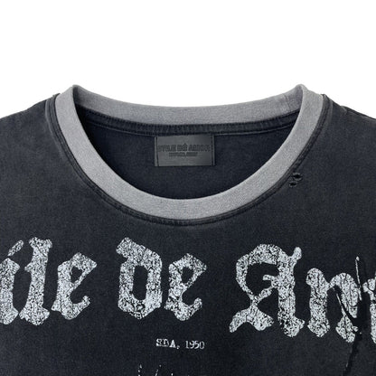 Close-up of a washed black t-shirt with a gray ribbed crew neck collar and a distressed white gothic text graphic reading 'ile de Ang' across the chest.