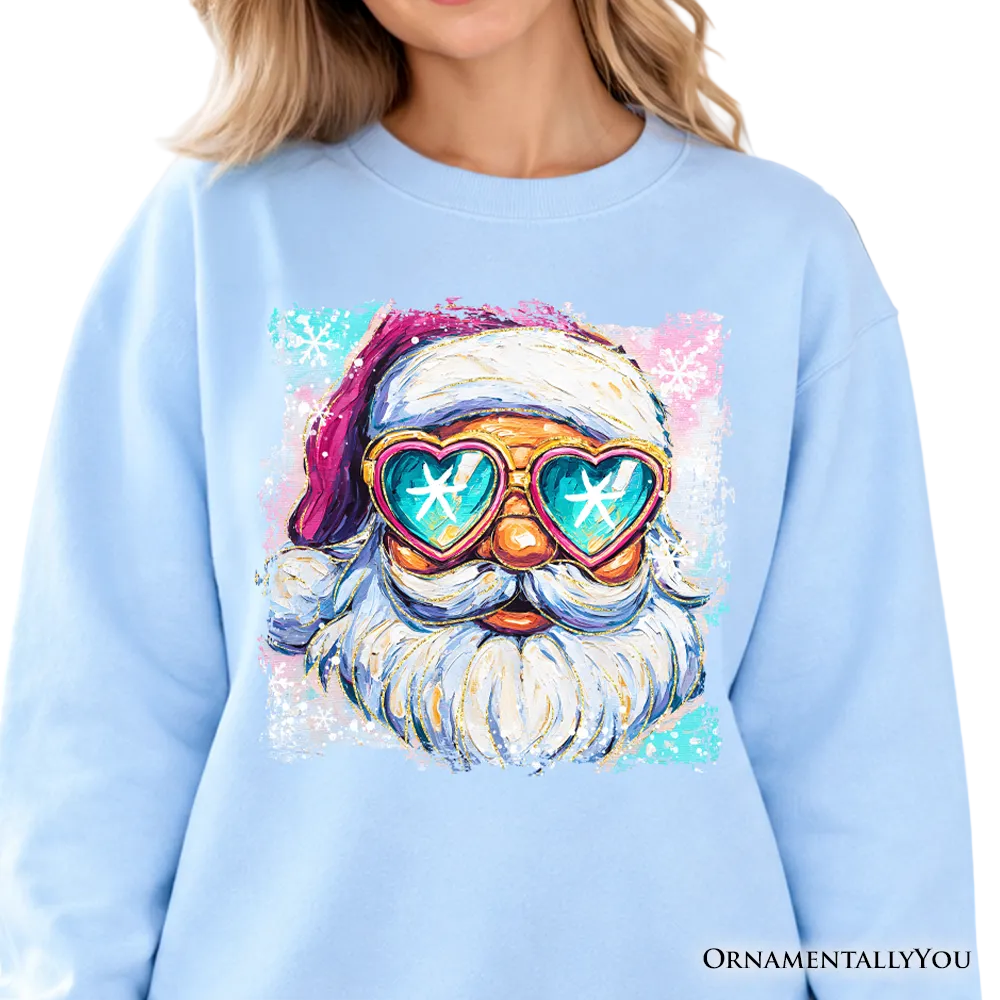 A person wearing a light blue sweatshirt with a colorful graphic of a Santa Claus face wearing heart-shaped sunglasses with snowflake reflections. The background is a softly blurred holiday interior with a decorated tree.