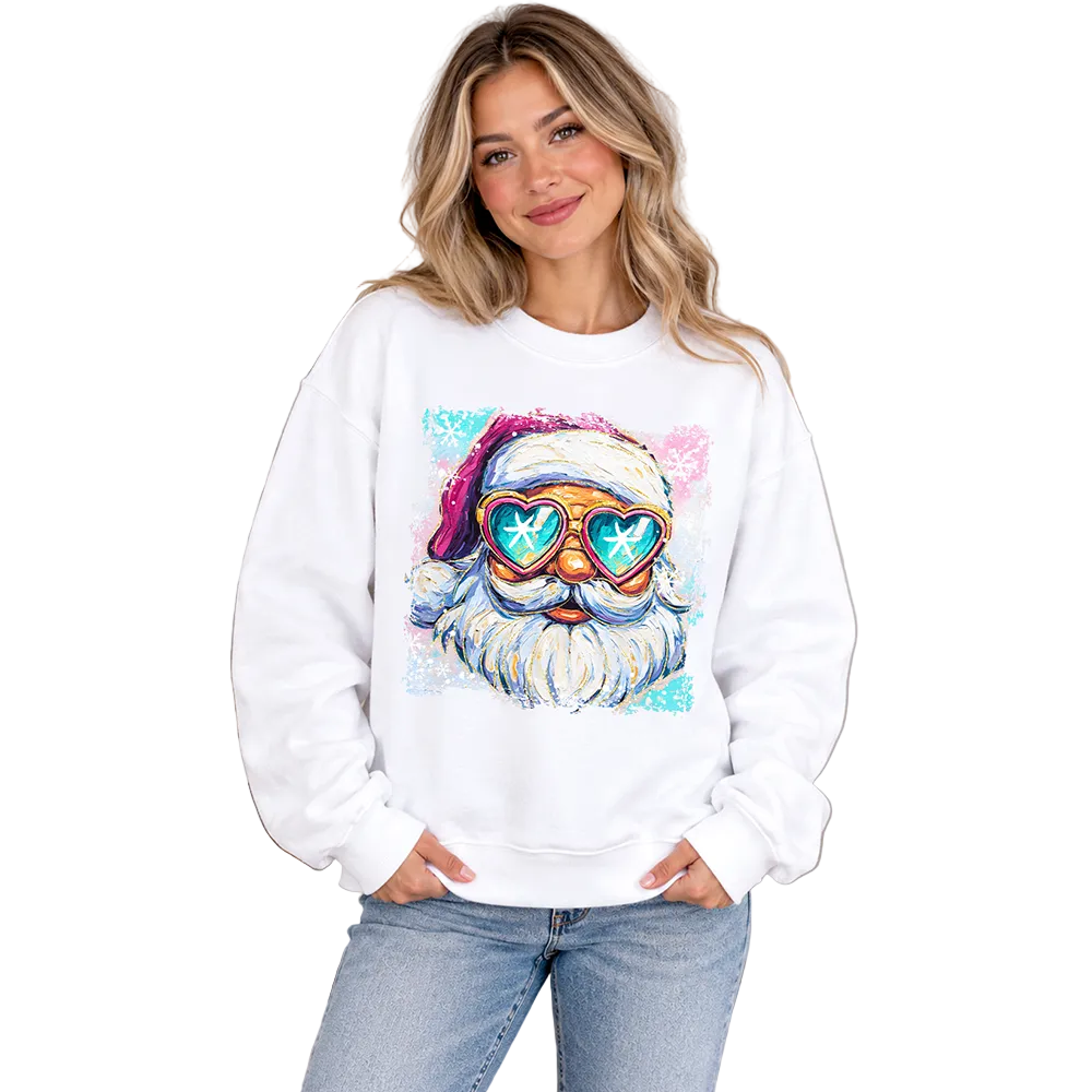 A woman wearing a white crewneck sweatshirt with a colorful graphic of a Santa Claus face wearing heart-shaped sunglasses, posed in a cozy, decorated living room.