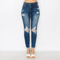 A model is wearing a pair of high-waisted, distressed blue denim jeans with ripped details at the knees and thighs, paired with white heeled sandals against a plain white studio background.