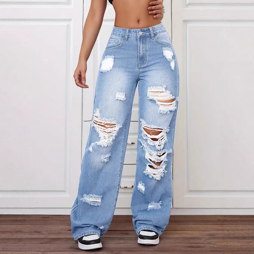 Ripped blue jeans worn by a person on a white paneled wall background