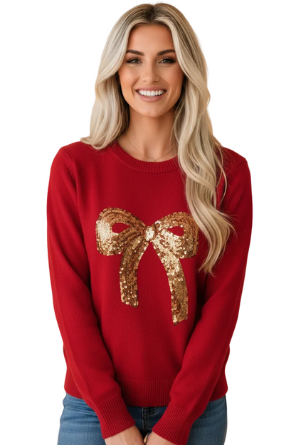 A smiling blonde woman wearing a red crewneck sweater with a large gold sequin bow graphic on the front, paired with blue jeans, set against a solid peach background.
