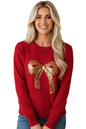 A smiling blonde woman wearing a red crewneck sweater with a large gold sequin bow graphic on the front, paired with blue jeans, set against a solid peach background.