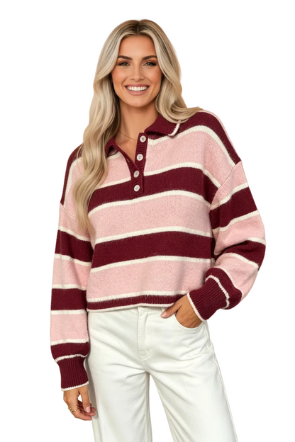 A smiling blonde woman wearing a pink and burgundy striped knit polo sweater with white pants, posed against a solid peach studio background.