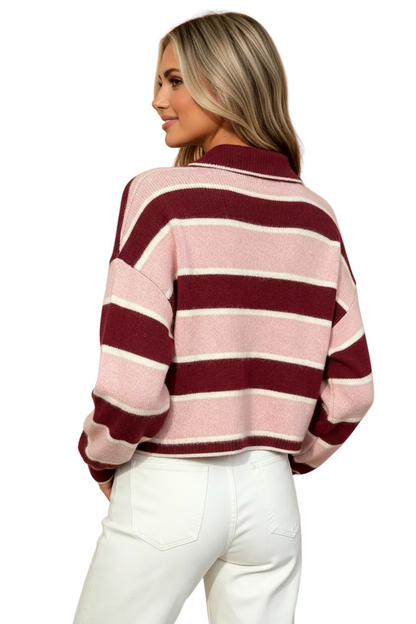 A woman shown from the back wearing a cropped knit sweater with horizontal stripes in dusty pink, burgundy, and off-white, paired with white pants, against a solid peach background.