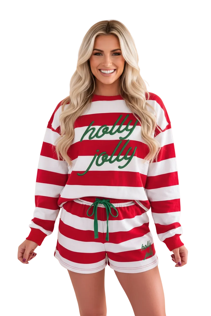 A woman modeling a matching holiday-themed loungewear set consisting of a red and white striped long-sleeve sweatshirt with green 'holly jolly' text, and matching red and white striped shorts with a green drawstring, set against a solid beige background.