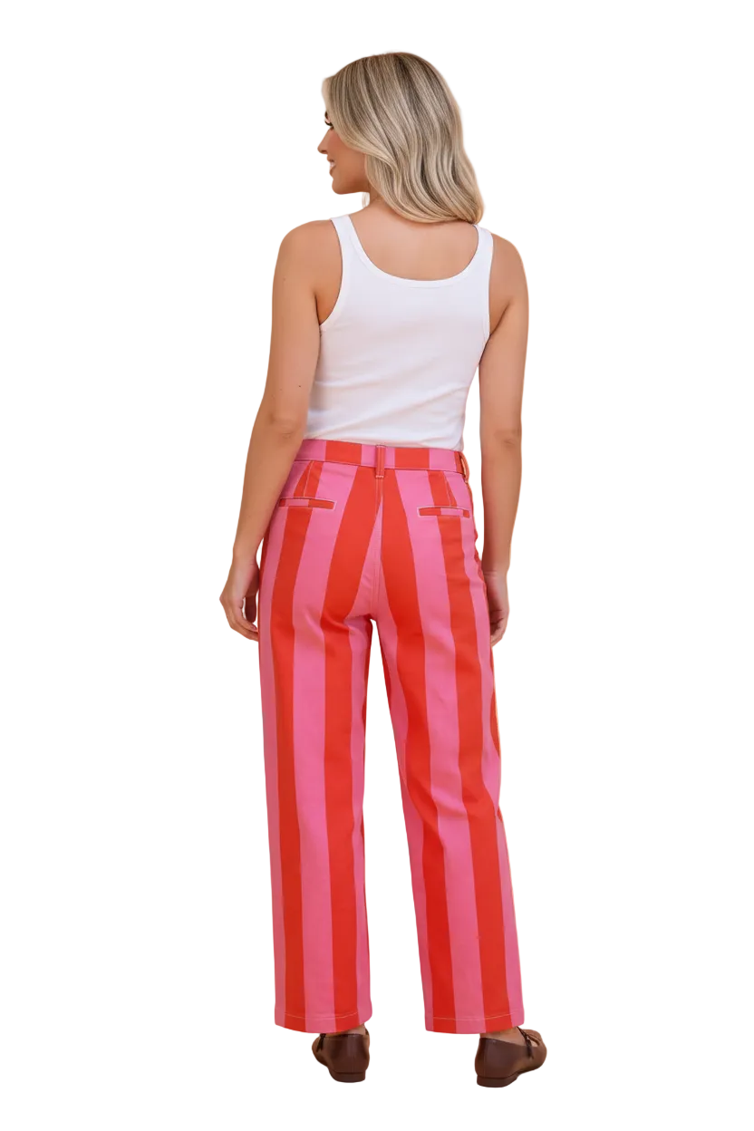 A woman shown from the back wearing high-waisted, wide-leg trousers with bold vertical pink and red stripes, paired with a white tank top and brown shoes, against a solid peach background.