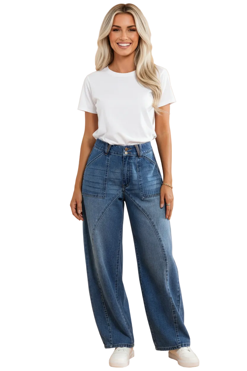 A woman modeling a pair of high-waisted, wide-leg blue jeans with a white t-shirt and white sneakers, standing against a solid peach-colored studio background.