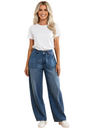 A woman modeling a pair of high-waisted, wide-leg blue jeans with a white t-shirt and white sneakers, standing against a solid peach-colored studio background.