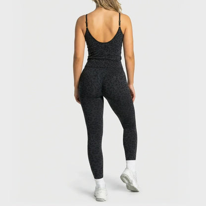 A woman shown from the back wearing a black leopard-print activewear set, consisting of a spaghetti-strap tank top and matching high-waisted leggings, paired with white socks and white sneakers, against a light gray studio background.