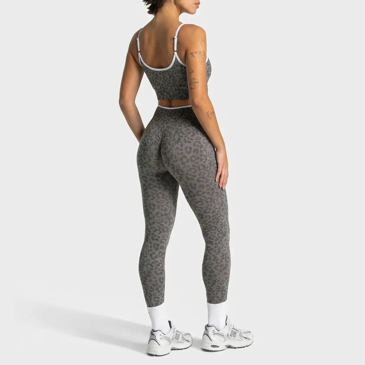 A woman shown from the back wearing a matching gray leopard-print activewear set, consisting of a sports bra and high-waisted leggings, with white socks and white sneakers, against a light gray studio background.