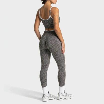 A woman shown from the back wearing a matching gray leopard-print activewear set, consisting of a sports bra and high-waisted leggings, with white socks and white sneakers, against a light gray studio background.