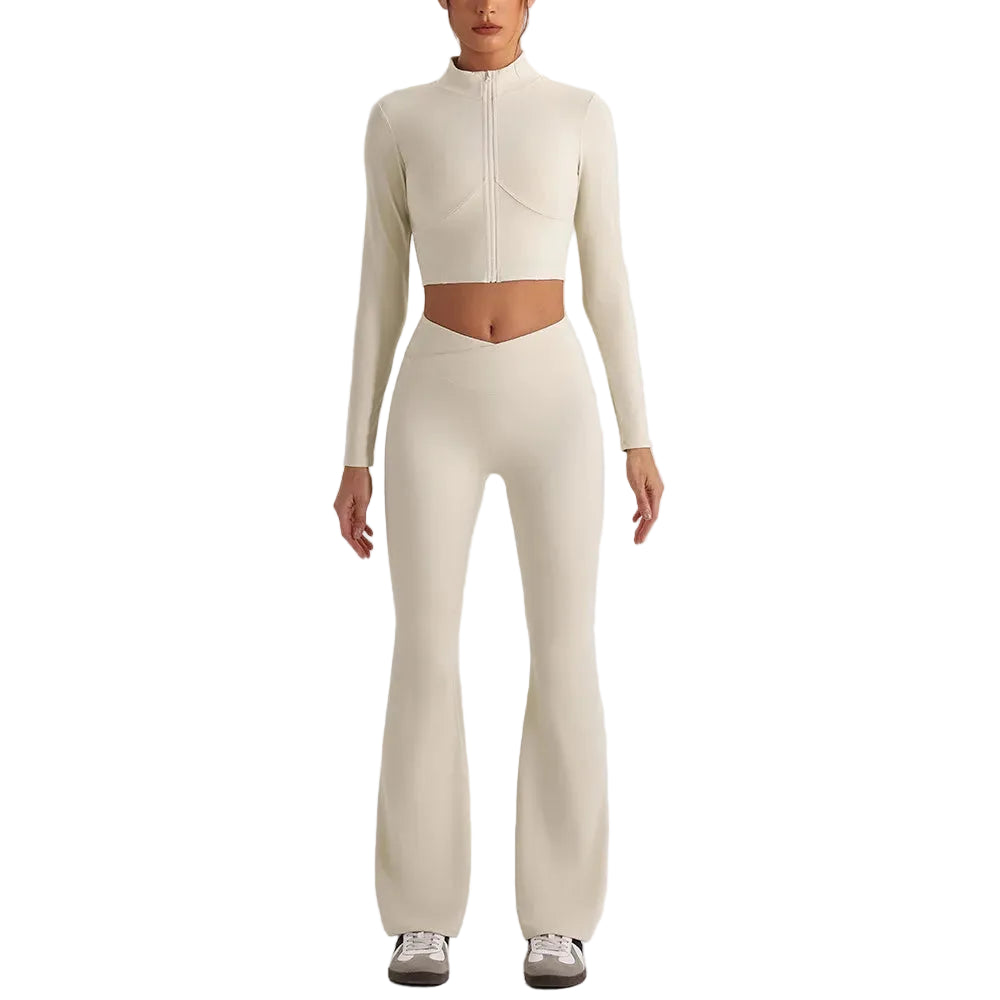 A model wearing a matching cream-colored two-piece activewear set consisting of a long-sleeve cropped zip-up top and high-waisted flared leggings, paired with white sneakers, against a solid light gray background.