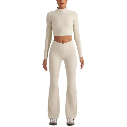 A model wearing a matching cream-colored two-piece activewear set consisting of a long-sleeve cropped zip-up top and high-waisted flared leggings, paired with white sneakers, against a solid light gray background.
